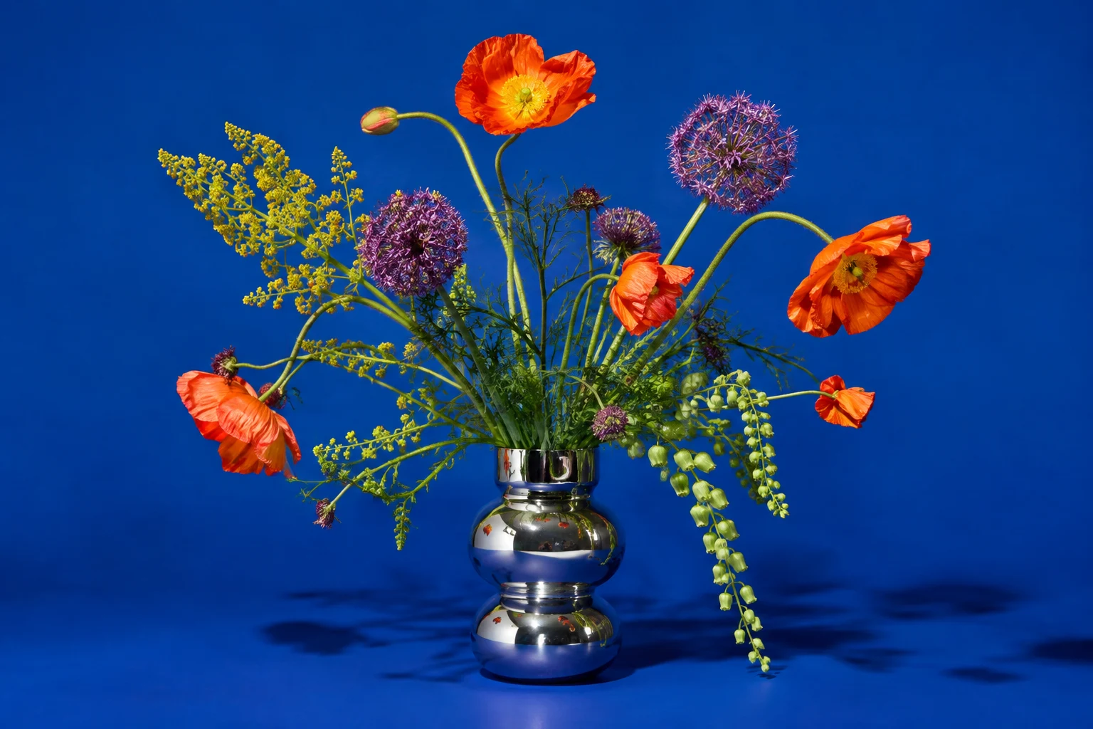 Pavots orange et fleurs violettes dans un vase chromé sur fond bleu