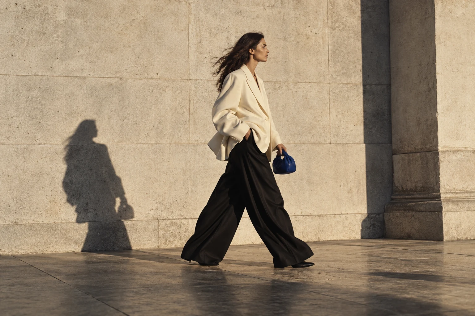 Silhouette en veste crème et pantalon noir devant une façade de pierre, image éditoriale de création